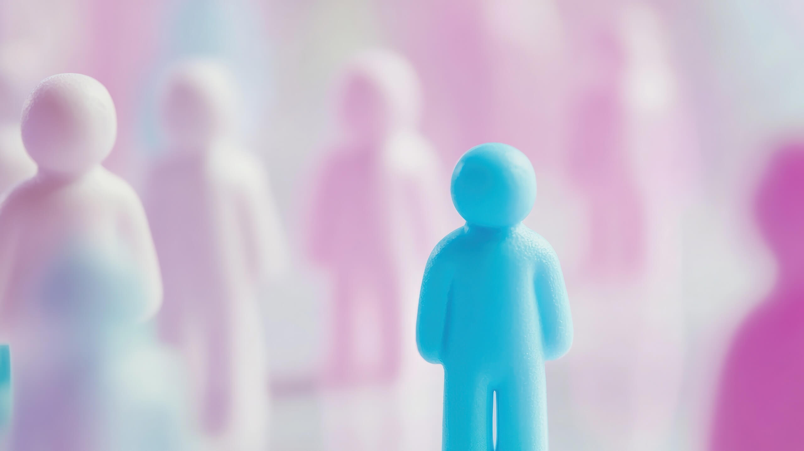 Blaue Figur aus Knetmasse im Vordergrund vor verschwommenem Hintergrund mit rosa und weißen Figuren.